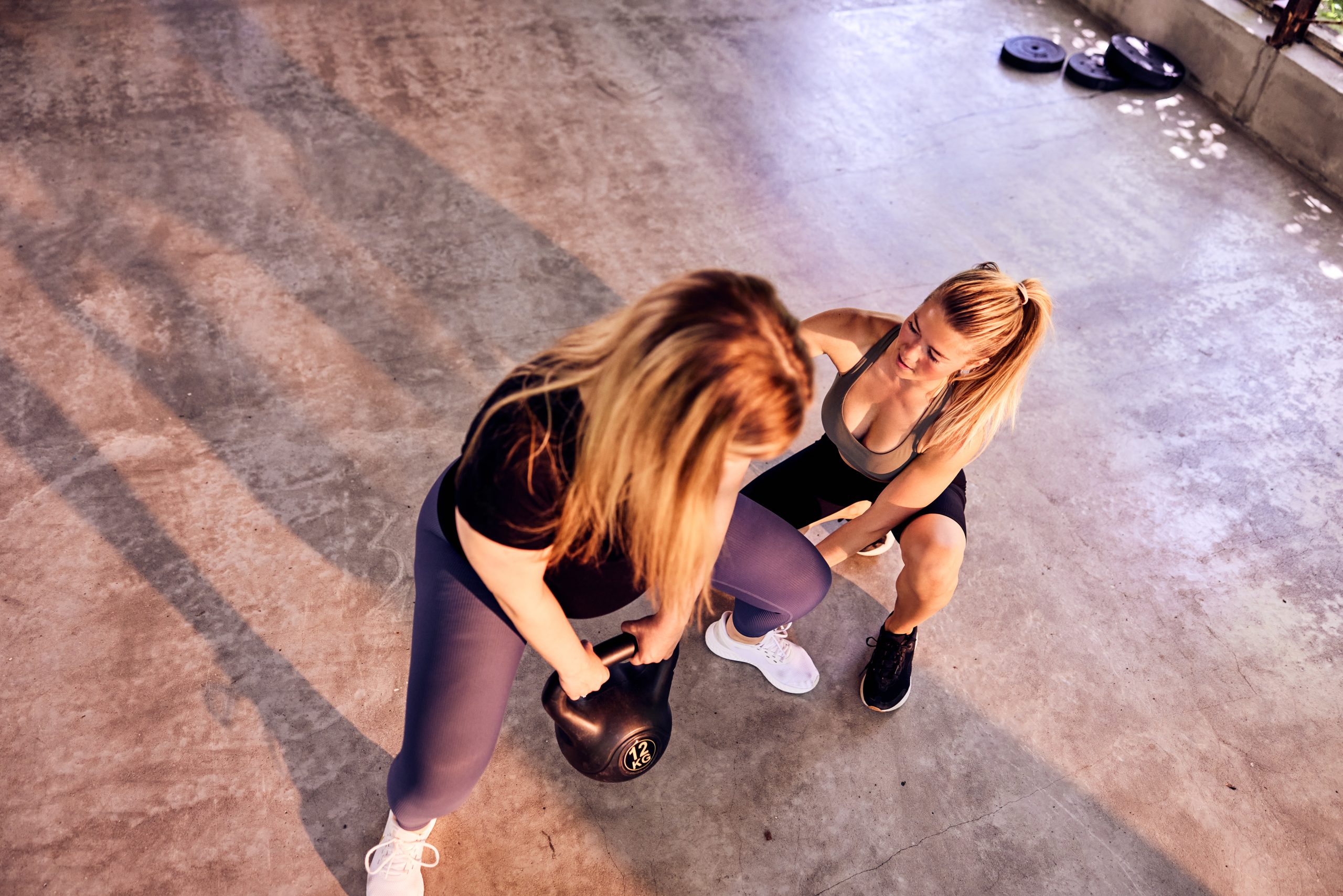 Instructor helping a woman lifting a kettlebell during a gym class