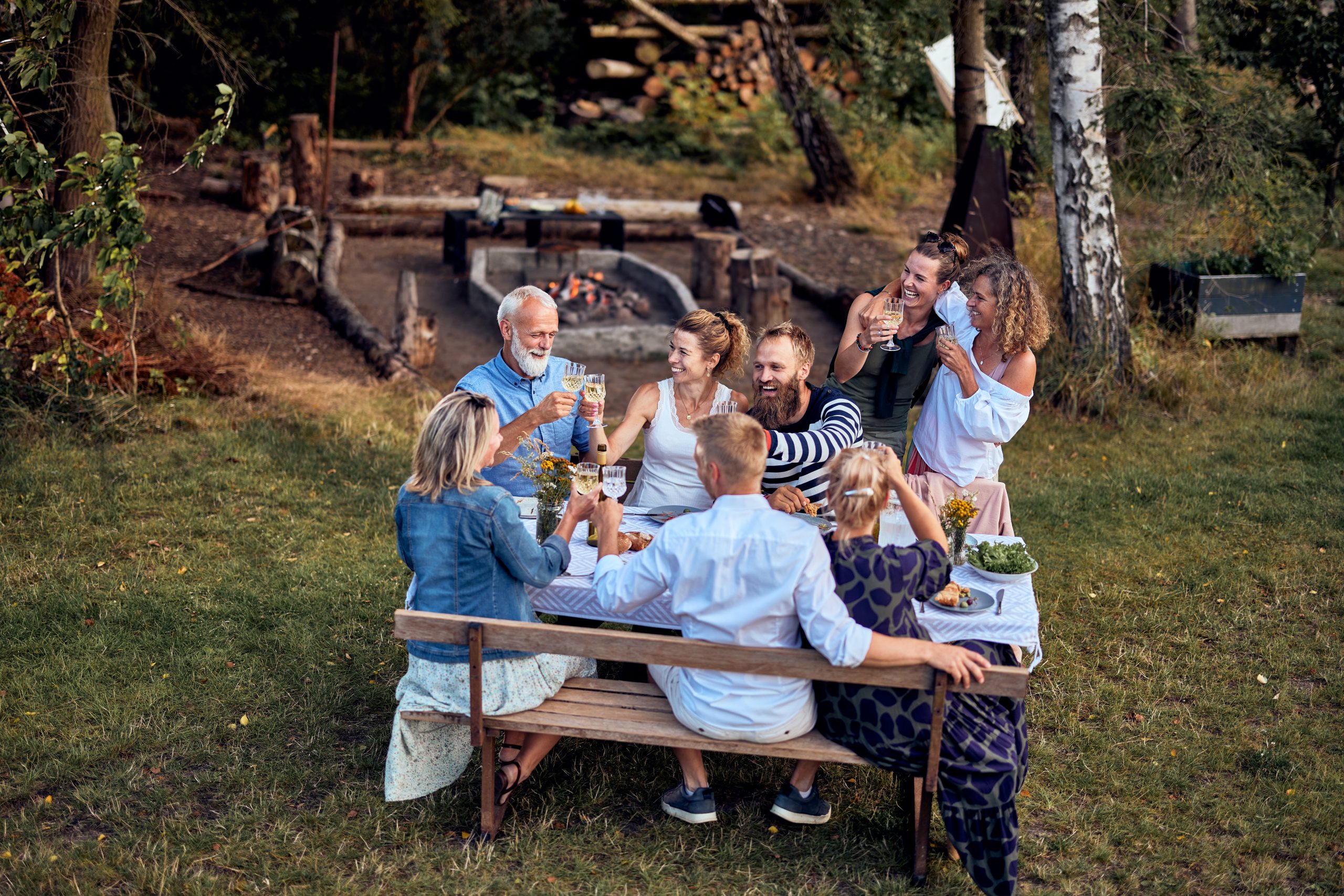 Smiling family and friends toasting each other with wine around a table outdoors in summer