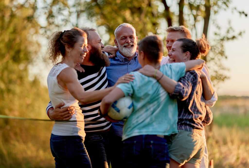 Laughing family hugging each other after playing a volleyball game outside in summer
