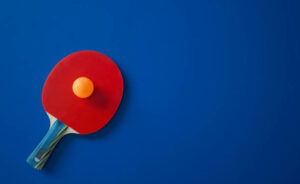 Red tennis racket lies on a blue table with a yellow ball