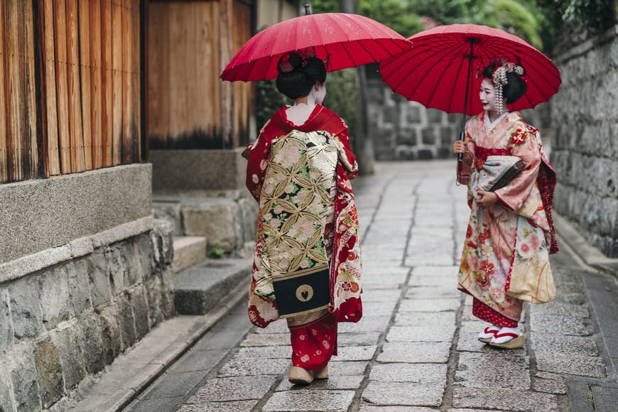 Maiko geishor med röda paraplyer som går på en gata i Gion i Kyoto, Japan.