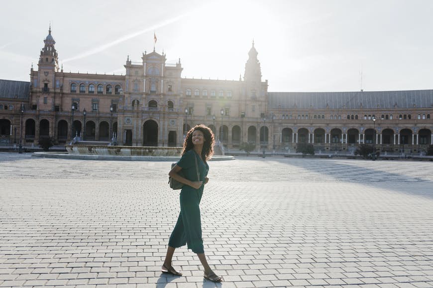 Leende ung kvinna tittar bort medan du går på Plaza De España, Sevilla, Spanien