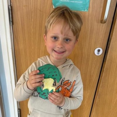 Photograph of boy with his handcraft paper egg in green with black spots and a gold centre.