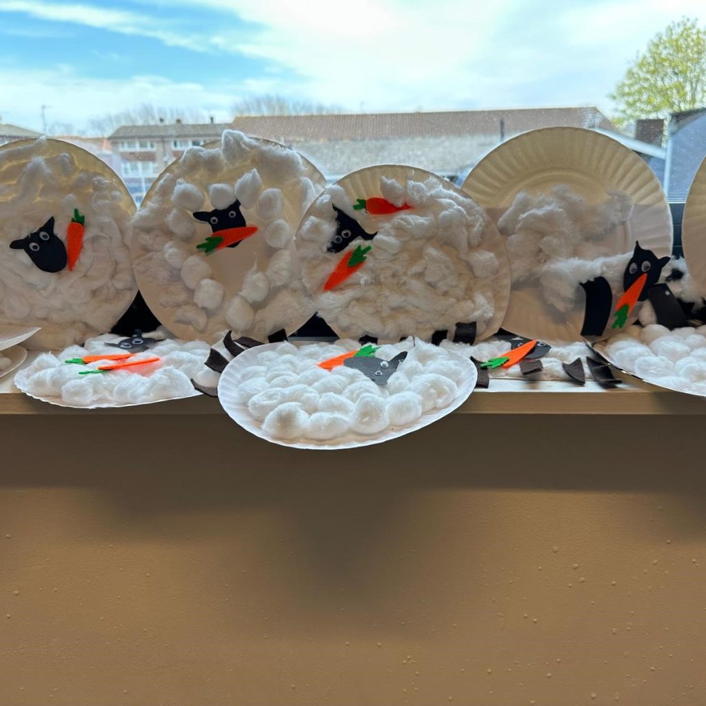 Photograph of series of paper plates on a window sill, with sheep designs made from cotton balls and black heads and carrots.