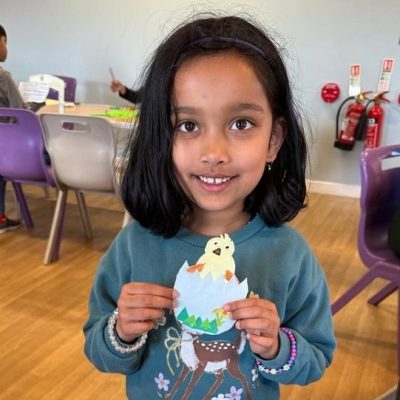 Photograph of girl showing her Easter egg craft. A blue egg with a duckling popping out.