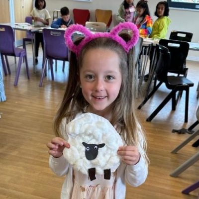 Photograph of girl wearing pink bunny ears holding a plate with a white sheep on it.