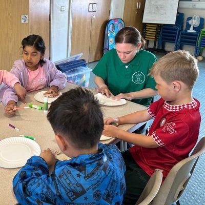 Photograph of children and play scheme worker concentrating on their plate decorating.