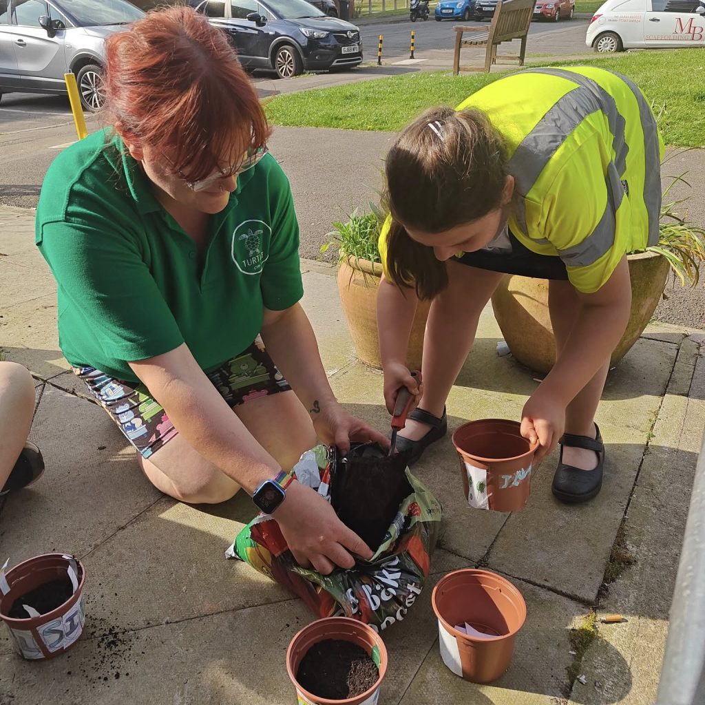 Photo of 1 girl and 1 play worker planting up pots.