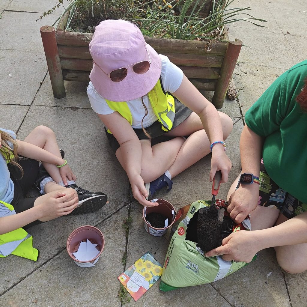 Photo of 2 girls and 1 play worker planting up sunflowers in pots.