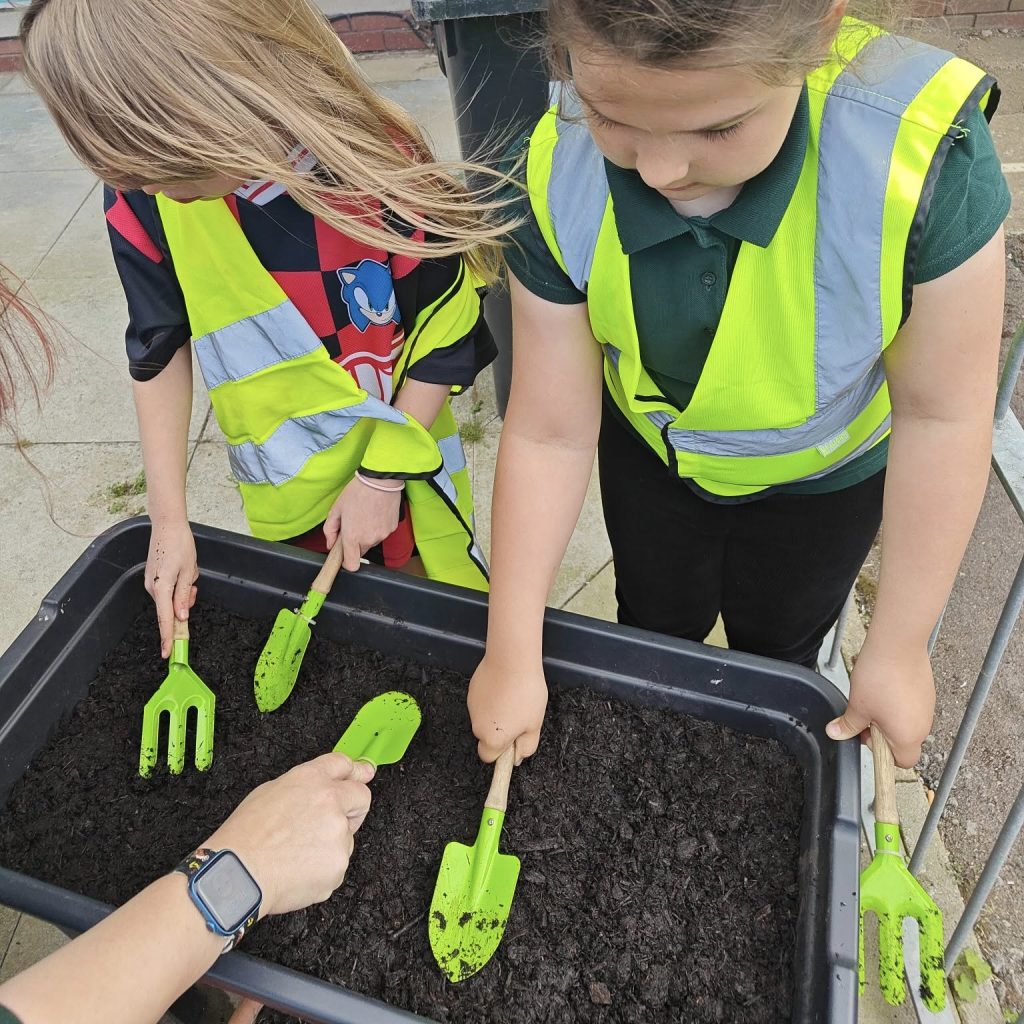Photo of 2 girls with mini trowels and forks patting down soil in a planter.