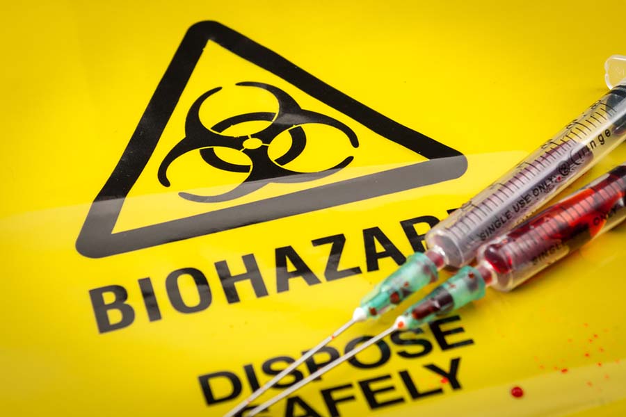 Blood filled medical syringes on yellow biohazard bag and spilled biological waste