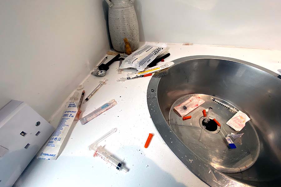 Hypodermic needles left around the edge of a sink containing a smattering of blood and other needles