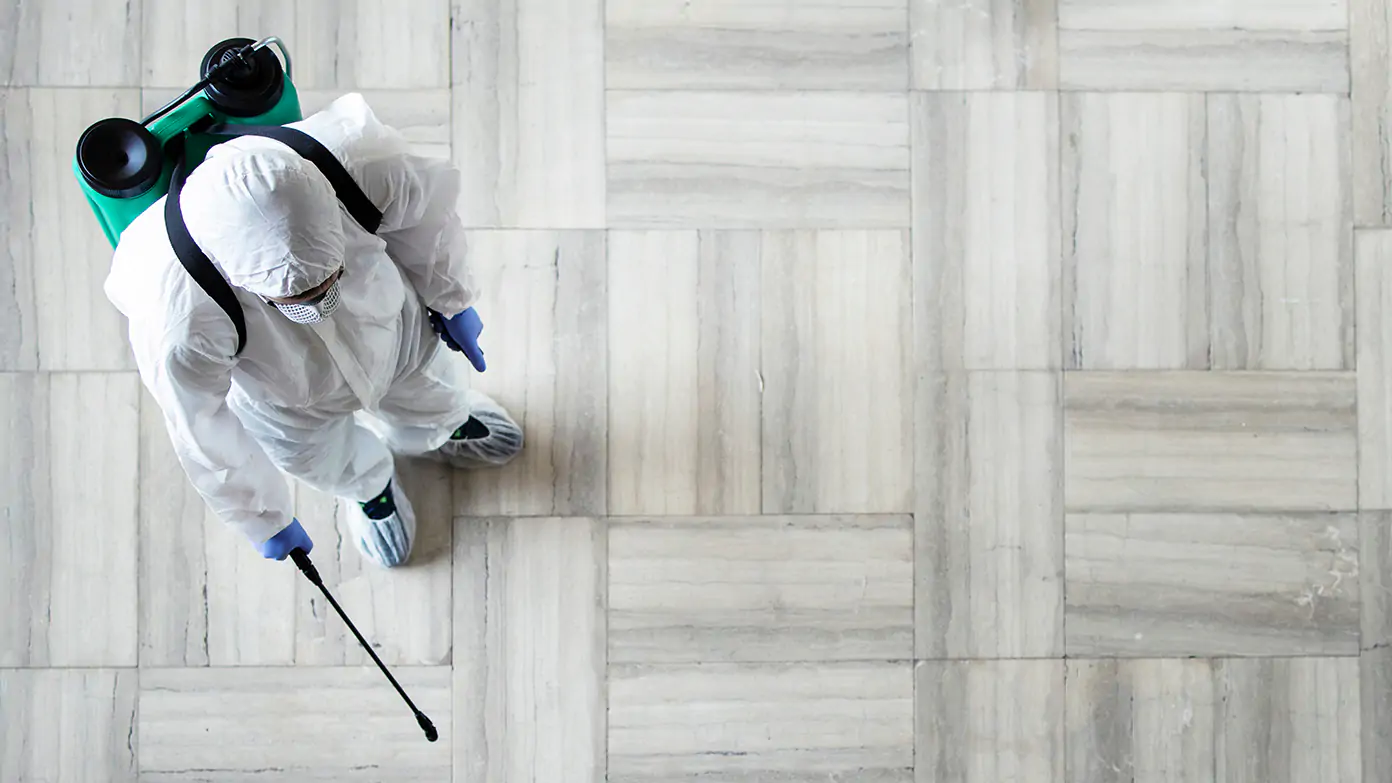 Cleaner wearing protective suit sanitising floor