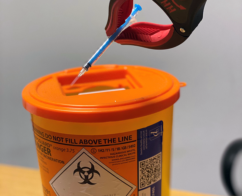 A hypodermic needle being safely disposed of