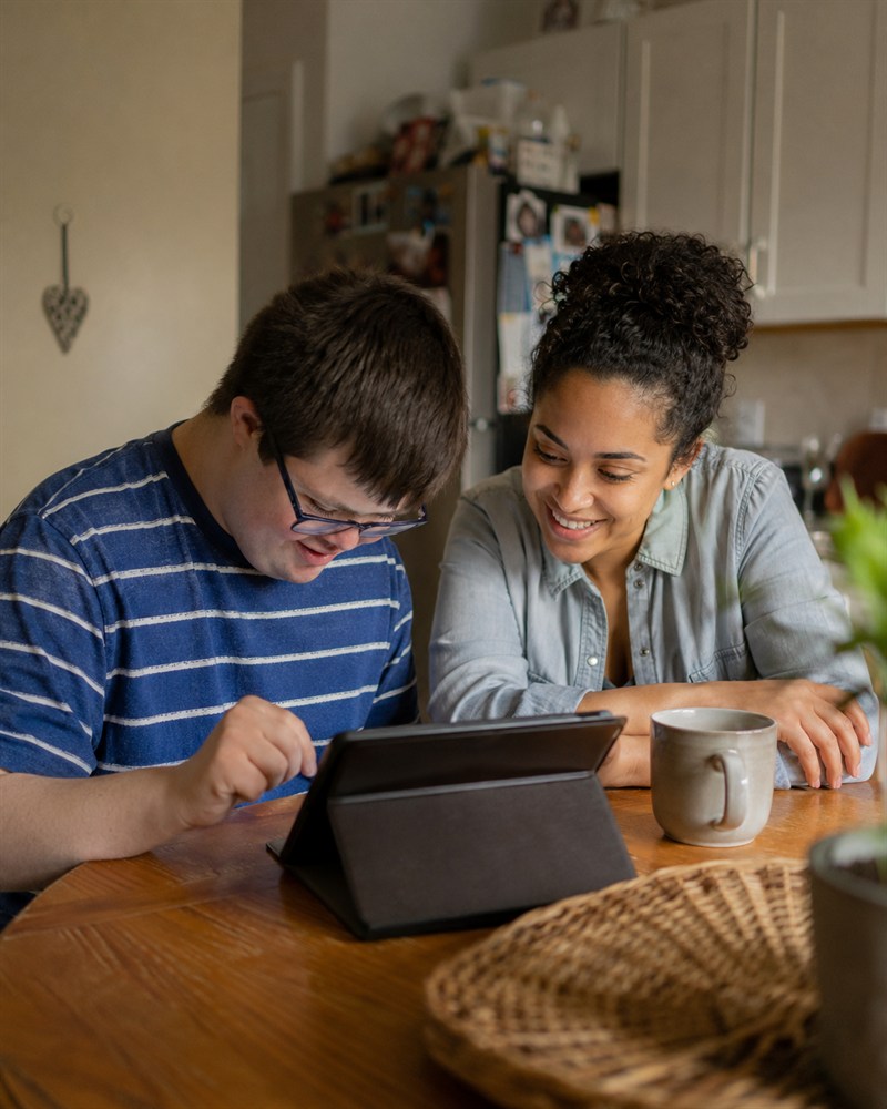 Young man with a learning disability and his support worker looking at a tablet together at a kitchen table