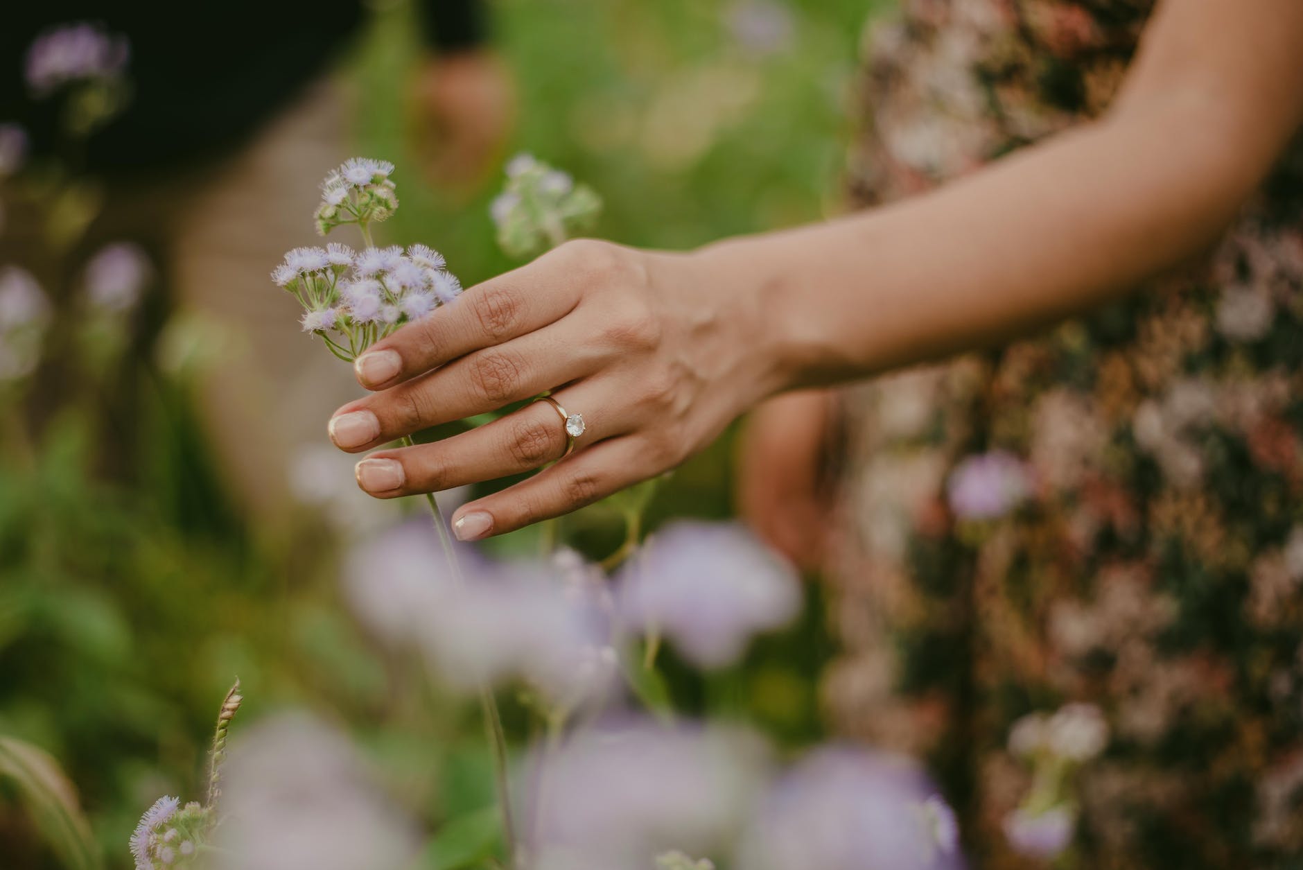 close up of woman wearing an engagement ring and touching a flower