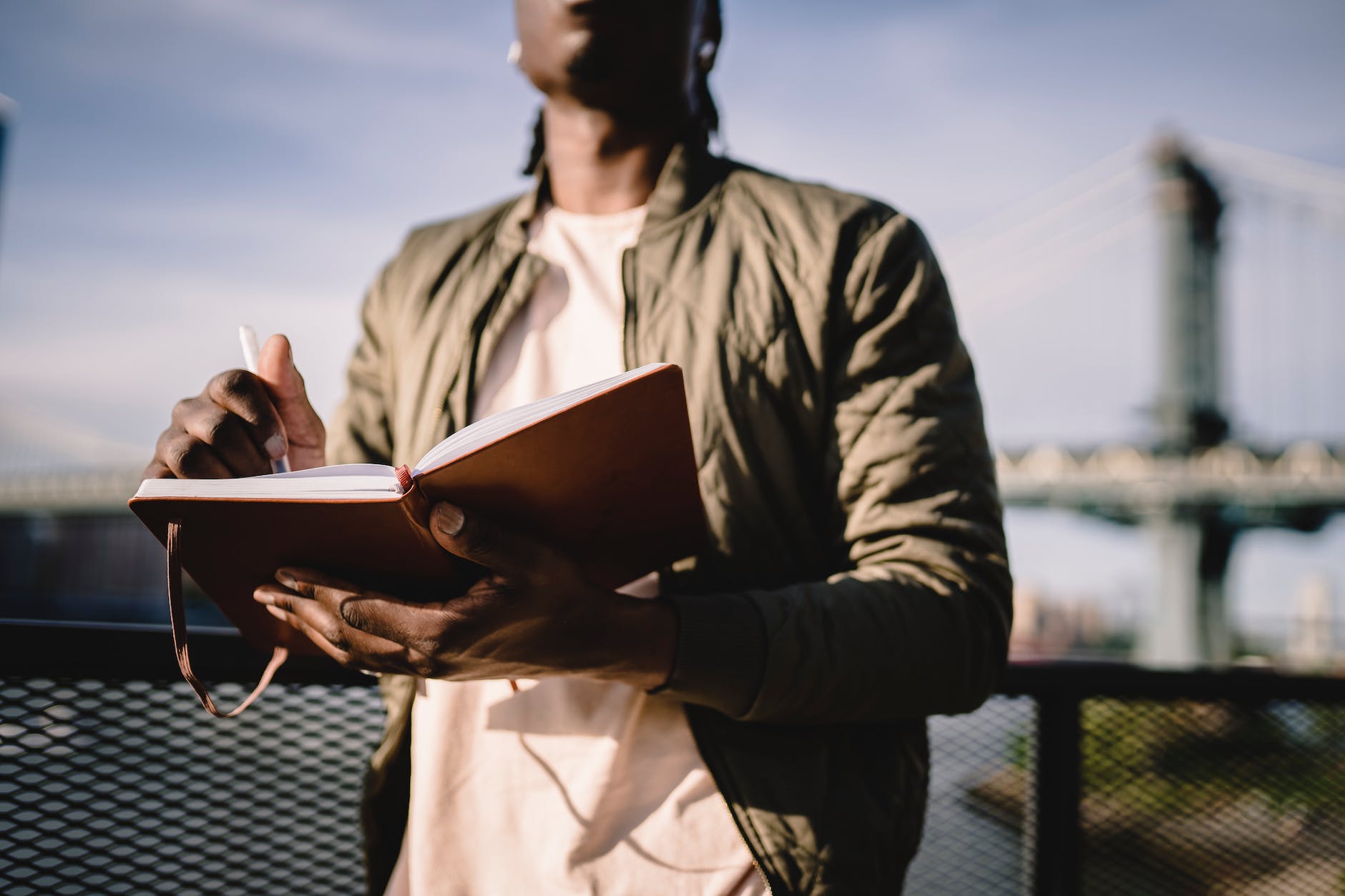 crop unrecognizable black man writing in notebook on balcony