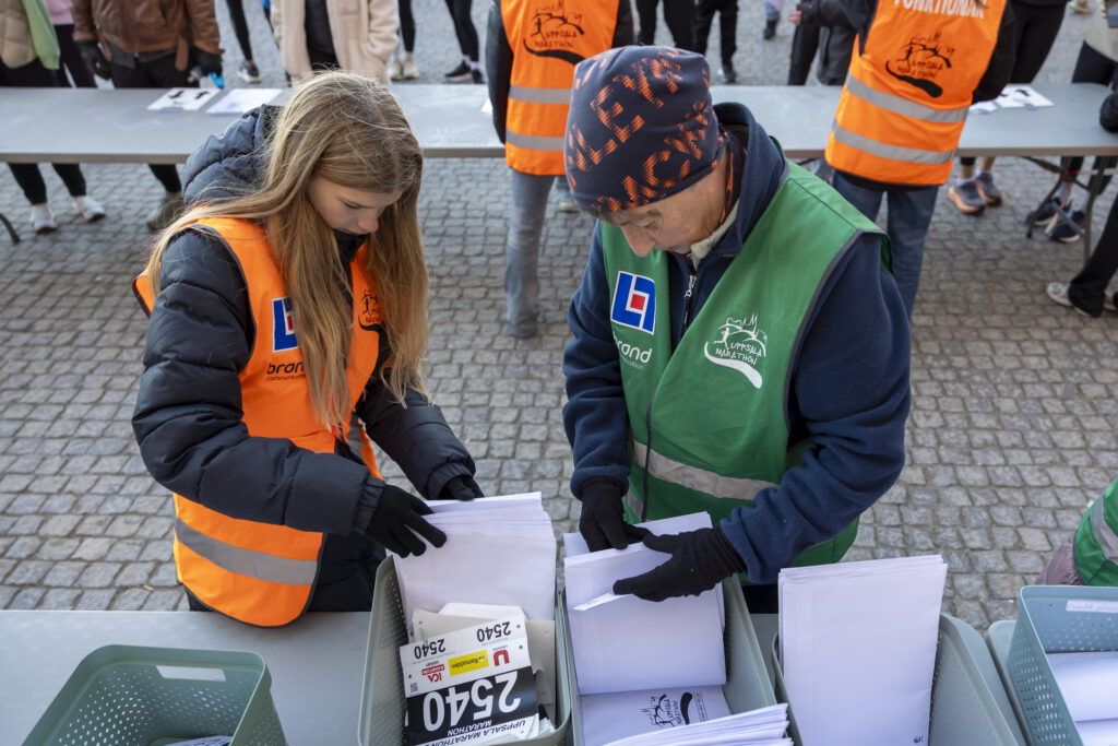 Bild på två funktionärer som delar ut nummerlappar - Uppsala Marathon 2025.