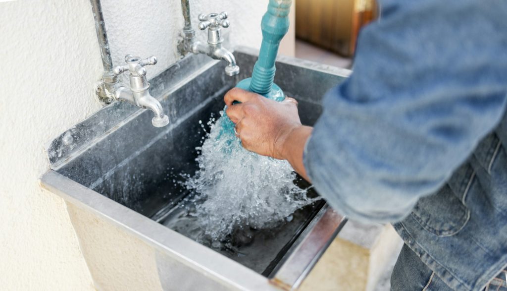 Plumber, water and man with plunger for kitchen sink, maintenance and repairs, blockage or cleaning