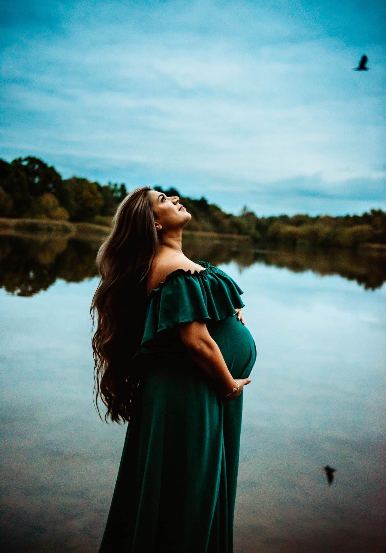 Woman pregnant standing on a lake holding her bely with West Sussex photographer aphy session