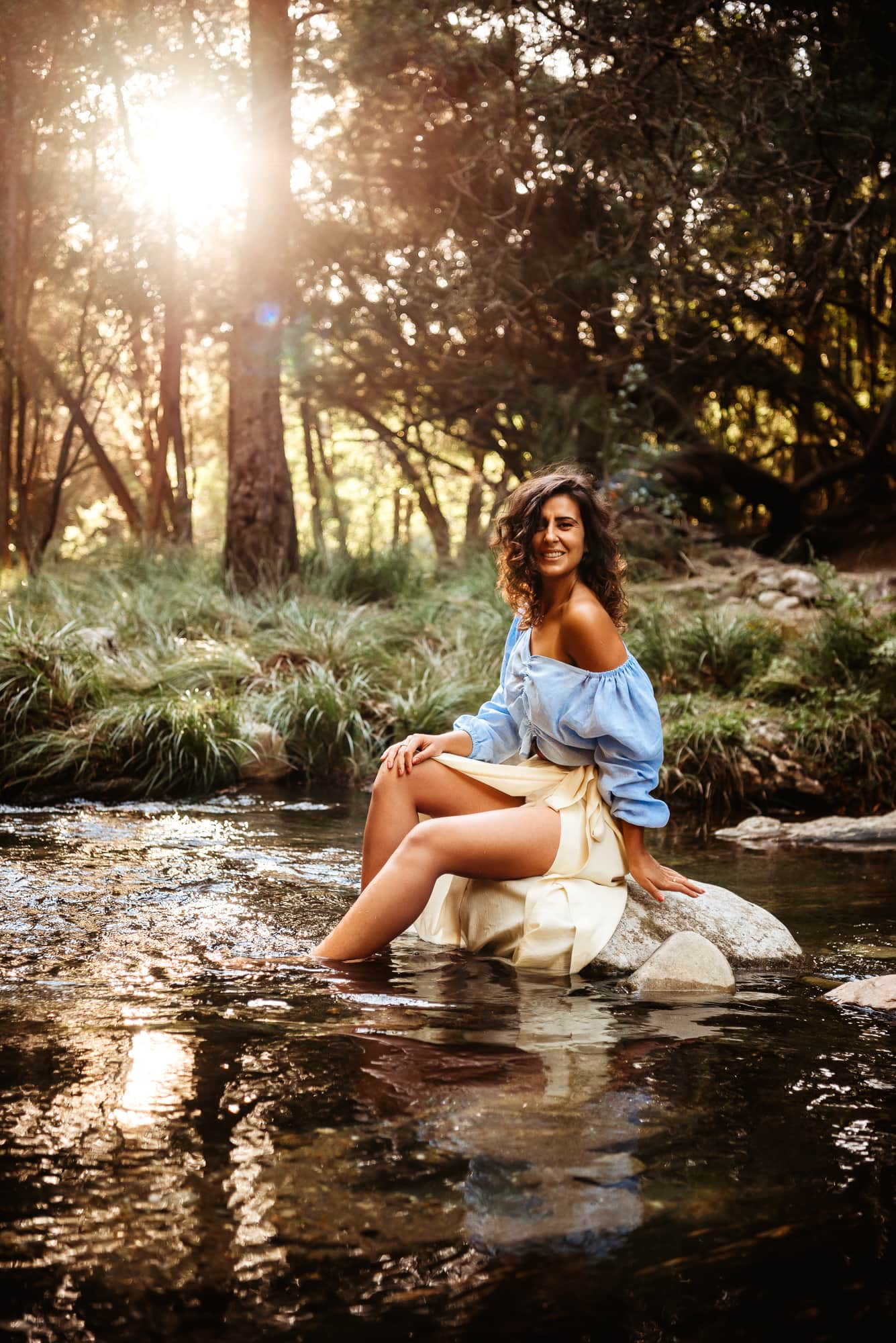 Woman sitting on a rock in a river with sunshine behind with west sussex female portrait photographer