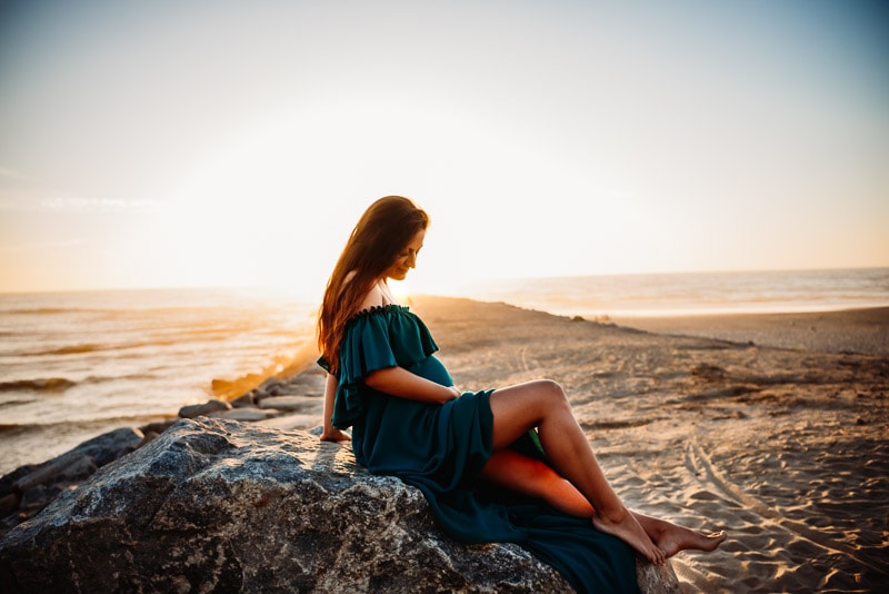 pregnant woman sitting on a rock with sunshine behind at maternity photography session