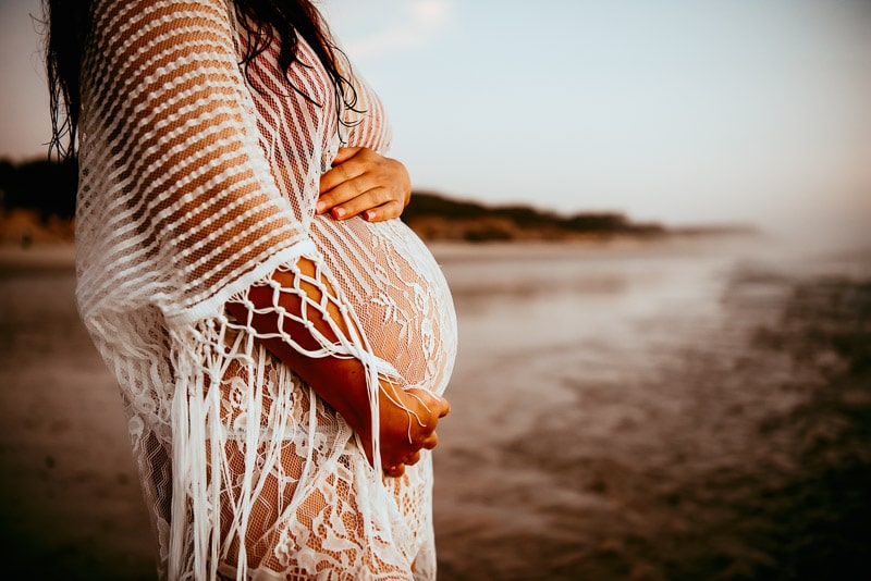 close up of a pregnant belly on the beach in West Sussex at Sunset with a maternity pregnancy session