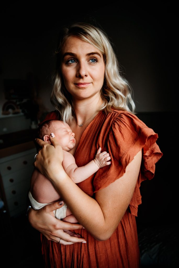 mum holding her newborn standing and looking out of the window at a newborn photoshoot