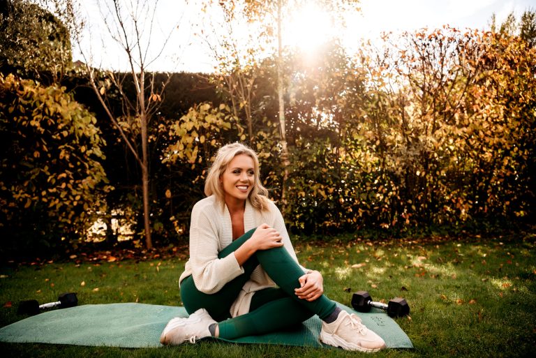Women posing in her yoga mat, sitting down and smiling