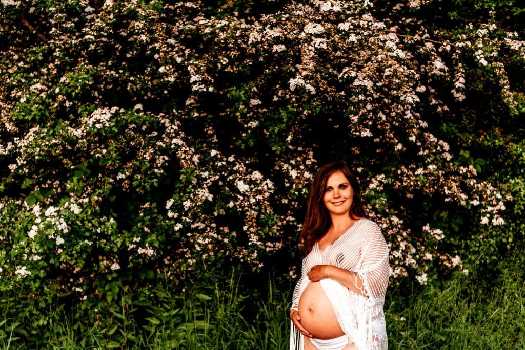 pregnant woman standing in front of flowers during a maternity photo session with vanessa gomes photography
