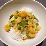 Eine Schüssel mit Reis und obendrauf ein Curry aus Blumenkohl, Zuckerschoten, Erbsen und Kokosmilch