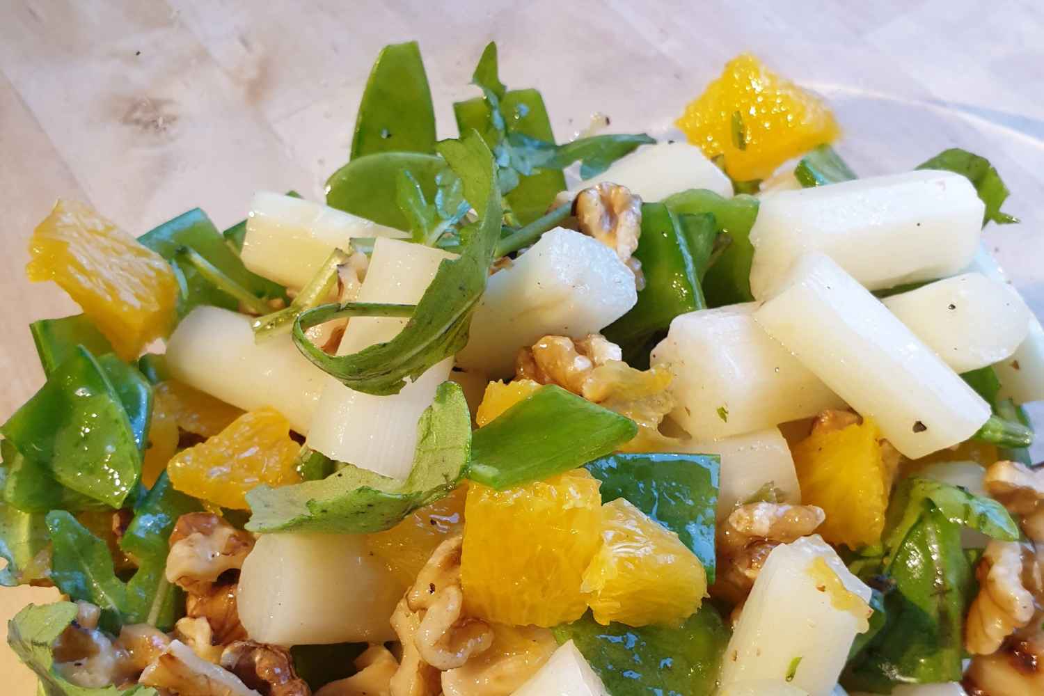 Auf dem Bild ist eine Schüssel Rucolasalat mit Spargel und Orangen zu sehen. Angereichert ist der Salat mit Walnüssen und Zuckerschoten