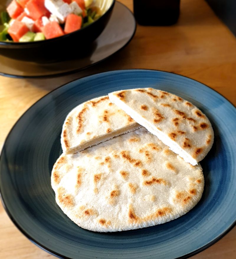 Auf einem Teller liegen zwei Scheiben Pfannenbrot und im Hintergrund steht ein Wassermelonen-Feta-Salat