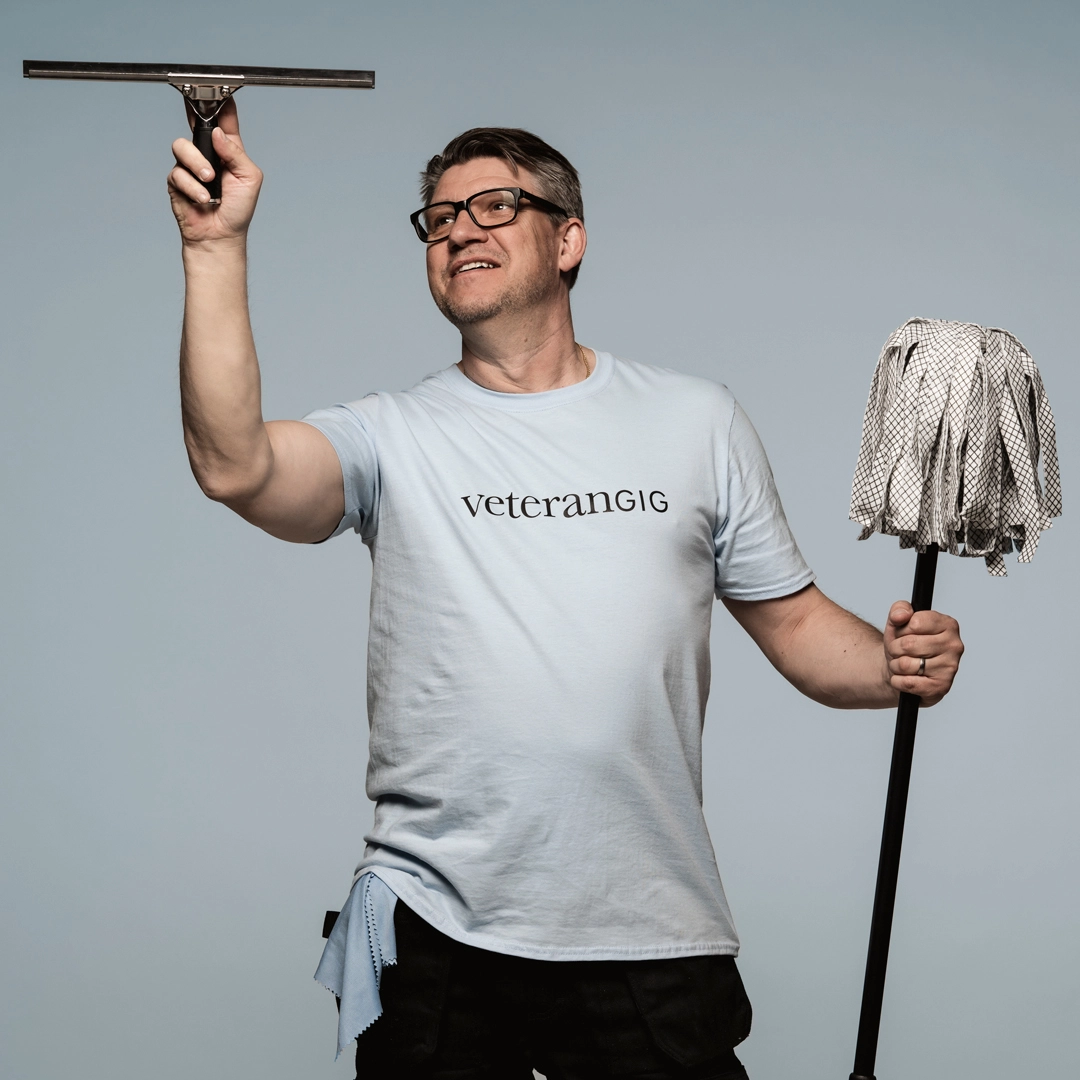 michell nordvall i ljusblå veterangig t-shirt. Städmopp i ena handen och en fönsterskrapa i den andra symboliserar att de utför städtjänster och fönsterputsning