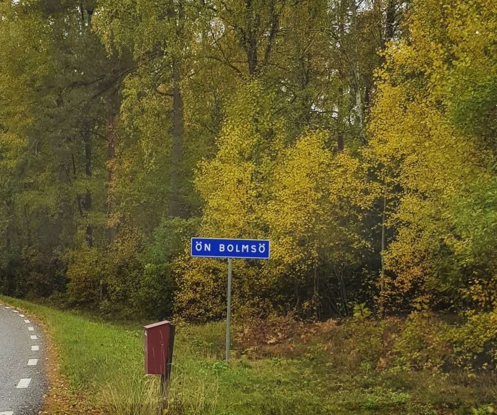 Gulnande höstlöv på träden med vägskylten "Ön Bolmsö" i förgrunden. Det var regnigt vid resan till Bolmsö, om än ingen höststorm.