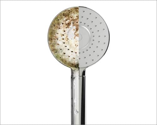Image of shower head half covered in grime and half pristine, demonstrating the impact of water softener installation