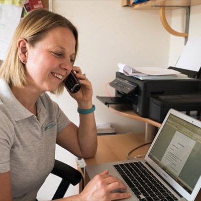 Image of Lindsey at her laptop and on the phone to a customer