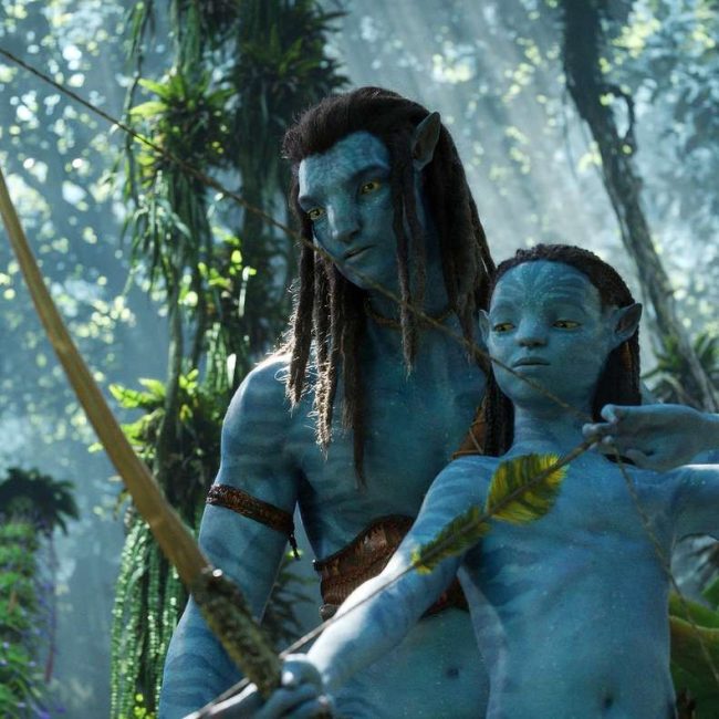 Bilden visar en scen från Avatar: The Way of Water där Jake står och lär ut pilbågsskytte till ett av sina barn.