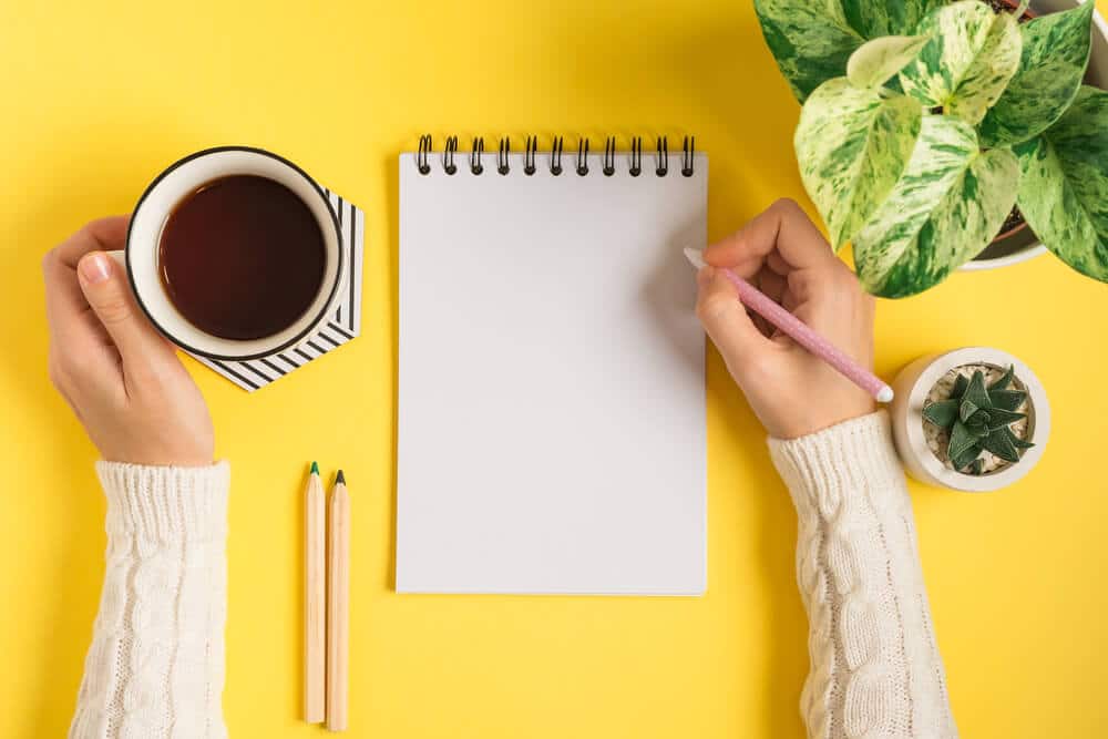 bloggen Jemand schreibt in ein Notizheft und hält eine Kaffeetasse