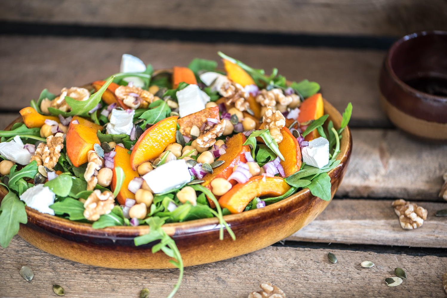 Liggend beeld van de pompoen salade met de dressing in een bakje ernaast