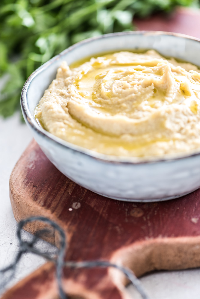 Foto van hummus met olijfolie en verse kruiden op de achtergrond