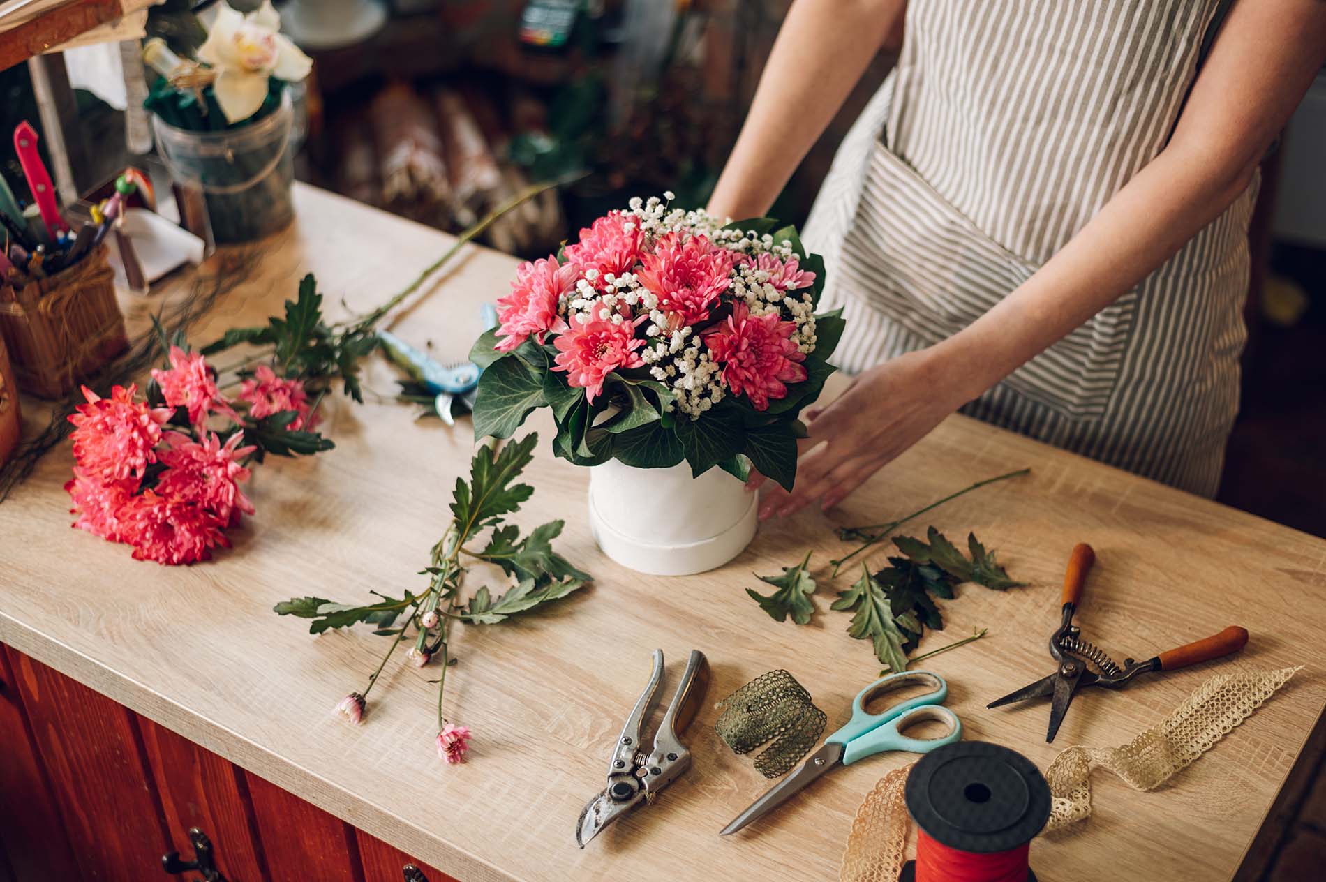 Die neue Kleinunternehmerregelung ab 2025 bringt erhebliche Erleichterungen und Vereinfachungen für Selbständige mit sich. Eine Floristin arrangiert rosa Blumenstrauß auf einem Holztisch mit Werkzeugen – Symbol für kreative Kleinunternehmer und Selbständige in Österreich.