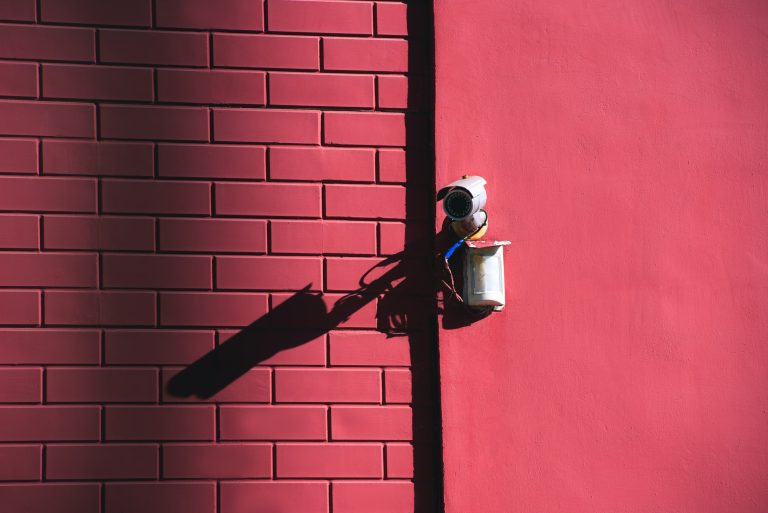 close up view of security camera on pink building facade in sunlight