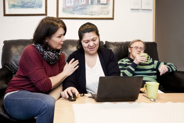 Healthcare worker helping woman with down syndrome in using laptop while man having drink at sofa