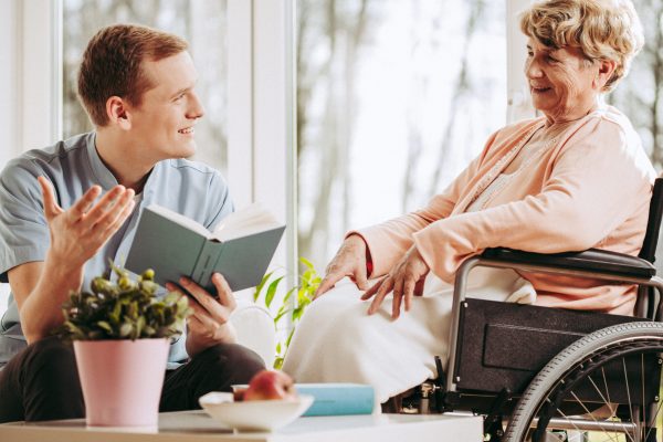 Older disabled woman on wheelchair spending time with male caregiver
