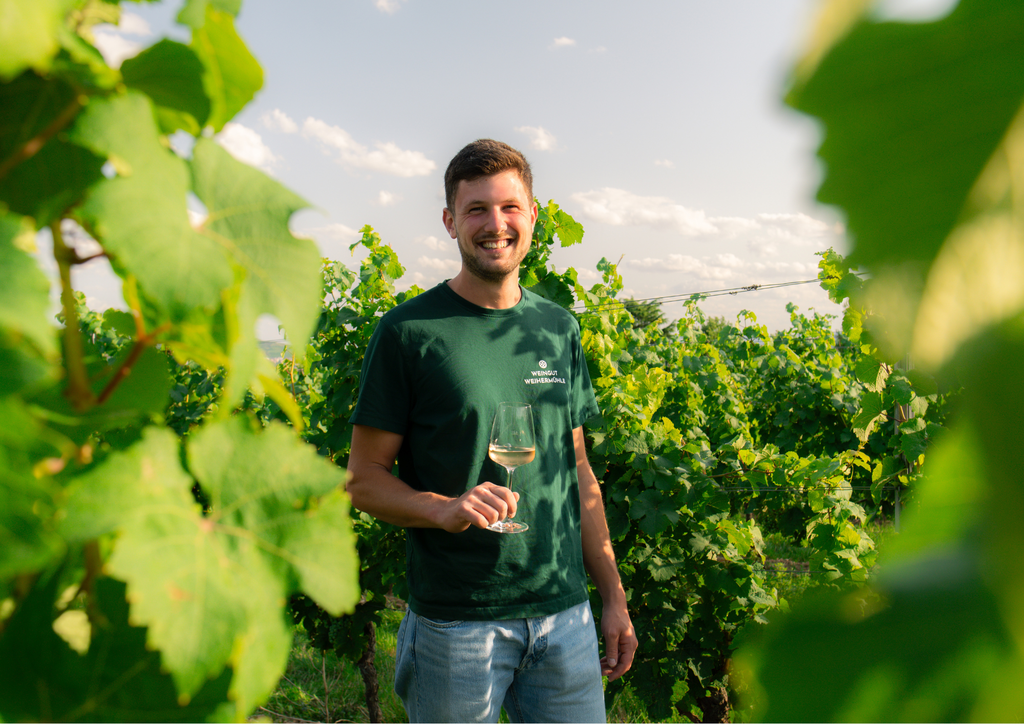 Jungwinzer Max Jung lachend mit Weinglas in den grünen Weinreben