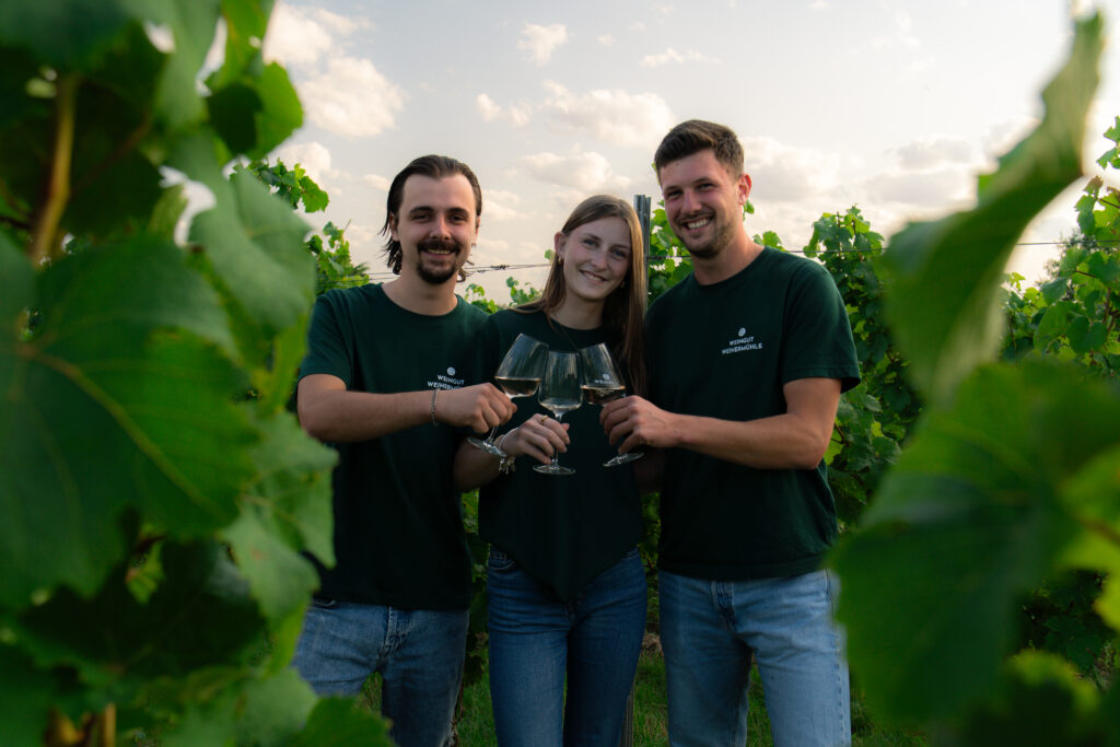 Tamara, Niclas und Max Jung mit Weingläsern in grünem Weinberg