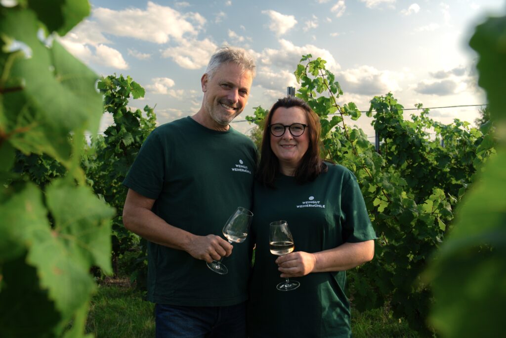 Nicole und Dirk Jung mit Weingläsern im grünen Weinberg