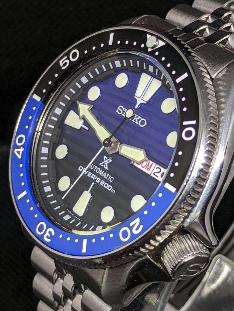 Seiko Mod by WellingTime UK. Batman Submariner SKX Mod: Flat sapphire crystal with blue AR coating, black Tuna chapter ring.  brushed SKX hands with C3 Lume mounted on a seiko Save the Oceans black to blue fade wave dial and Seiko NH36 movement. SKX Coin edge bezel fitted with a flat batman bezel insert black and blue in colour with a pearl of lume at noon. The watch sits on the wrist witha stainless steel seiko jubilee strap