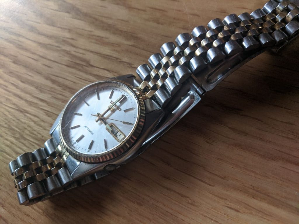 Wellingtime UK watch repair, Seiko DateJust before repair - This is a Broken Watch. The watch is stainless steel with gold fluted bezel Movement not working. replace Broken glass (hair line fracture to crystal. Dial feet replacement required. The Seiko 7009 3110 is on the original Bi-metal coloured jubilee bracelet. 